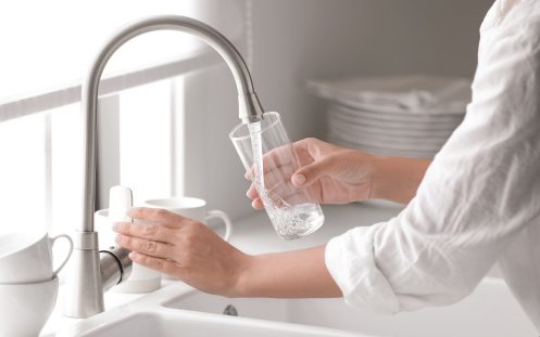 Moteris pila vandenį į stiklinę iš krano