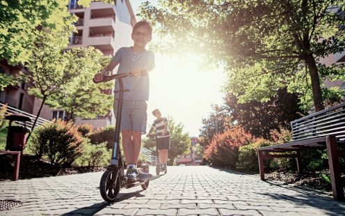 Vaikai važiuoja su paspirtukais mieste